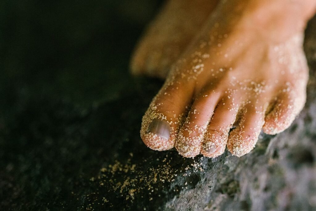 A close-up shot of a sandy human foot resting on a dark textured surface.